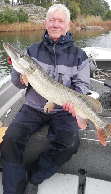 a man is sitting in a fishing boat in sweden, he caught a pike in sweden.