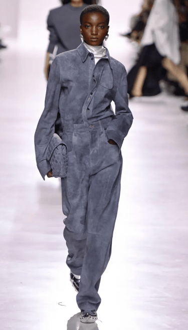 Bottega Veneta Spring/Summer 2026 Slate blue suede jumpsuit with woven clutch. 