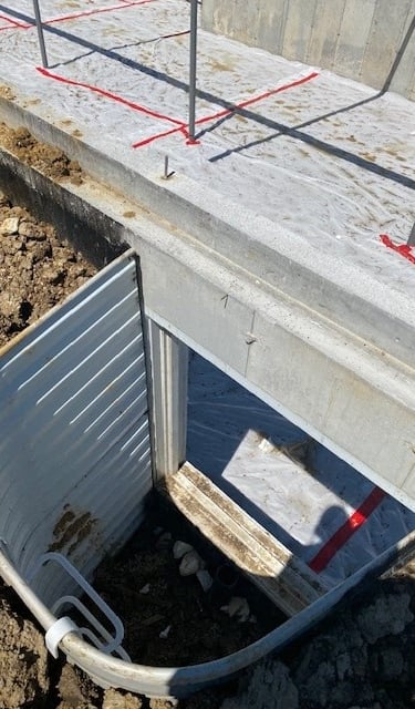 Egress window well installed against a concrete foundation on a construction site.