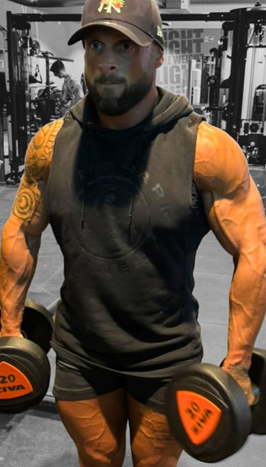 Romain Pittier, coach sportif musclé en salle de sport, tenant des haltères de 20 kg, prêt à guider ses clients vers leurs ob