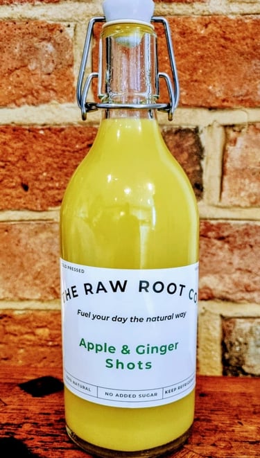 Apple & Ginger health and wellness shots in a glass swing top bottle from The Raw Root Co. Displayed on a wooden table.