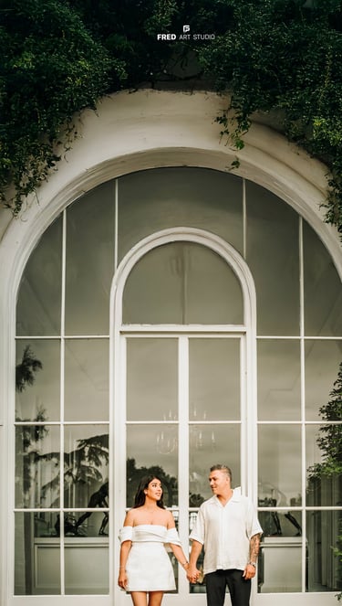 Couple holding hands in front of large white window – engagement photography by Fred Art Studio