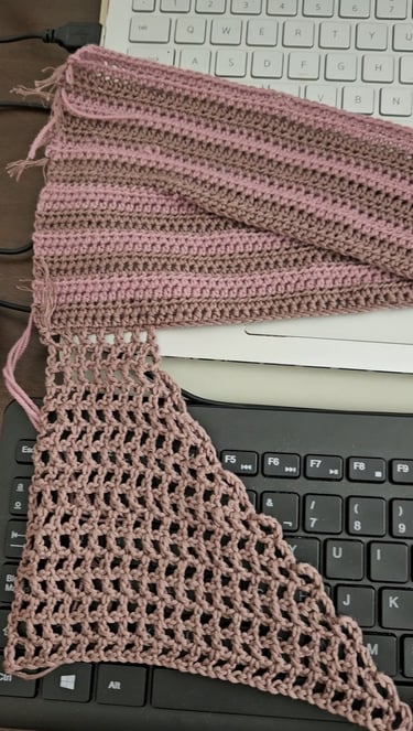 Pink and brown handmade crochet fabric swatches resting on a laptop and computer keyboard.