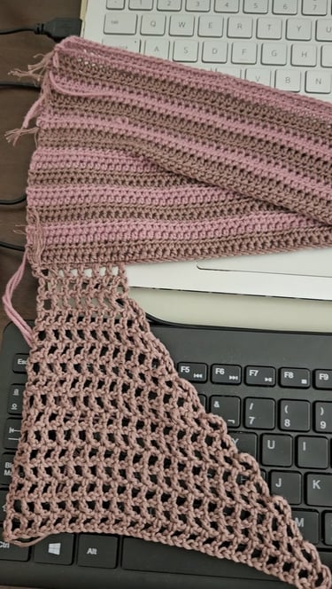Pink and brown handmade crochet fabric swatches resting on a laptop and computer keyboard.