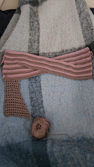 Handmade pink and brown striped crochet scarf project resting on a wool blanket with a ball of yarn.