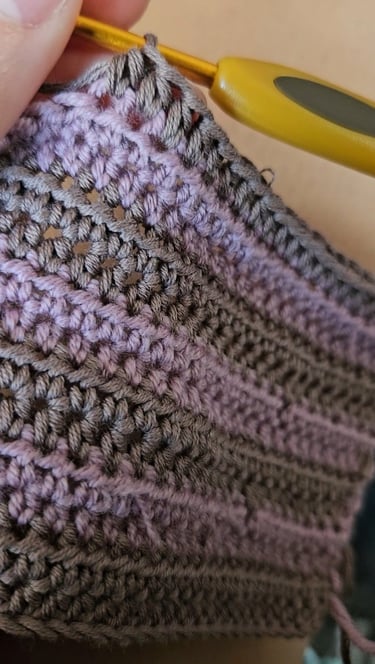 Close-up of a yellow crochet hook making stitches in purple and grey yarn fabric.