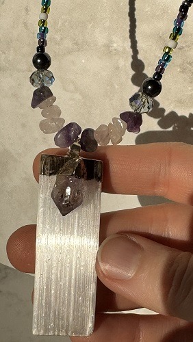 A crystal necklace with a shiny pendant made from selenite with an amethyst fixed on top