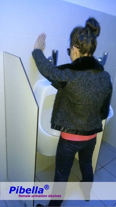 A woman urinates standing with a Pibella FUD into a urinal.