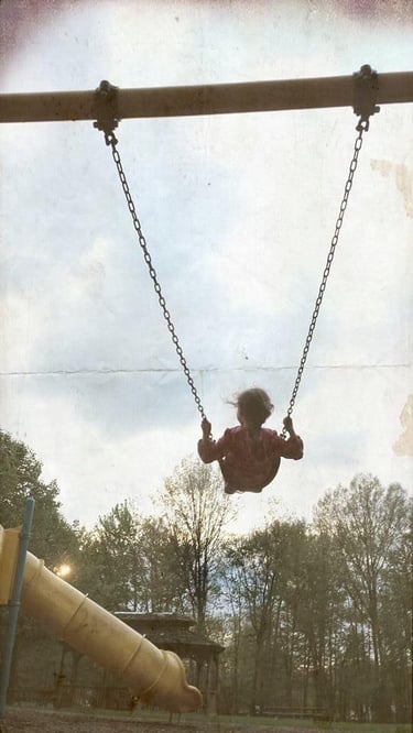 Girl swinging on a playground with trees in the background