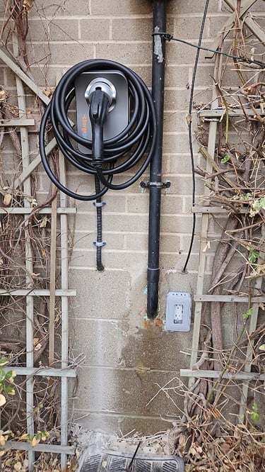 A ChargePoint home EV charger installed on an exterior brick wall with coiled black charging cable.
