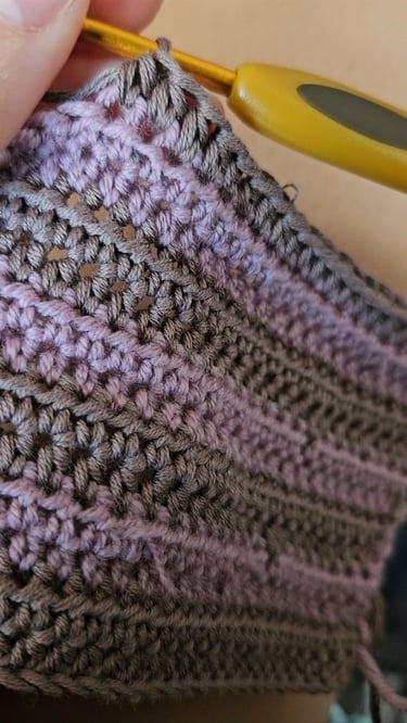 Close-up of a yellow crochet hook making stitches in purple and grey yarn fabric.