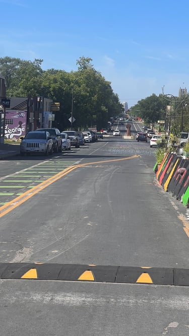 Sunny city street in George Floyd Square with colorful barriers and parked cars under a blue sky.
