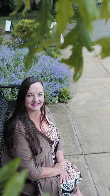 Photo of RuthAnn Lander smiling on a bench under a tree