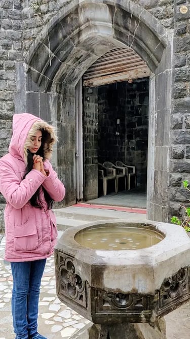 Visitor tossing a coin into the wishing well at St. John in the Wilderness Church, McLeod Ganj.