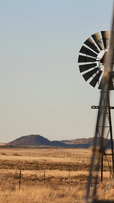 Windmill with trough in the middle of a dry landscape with some hills in the back