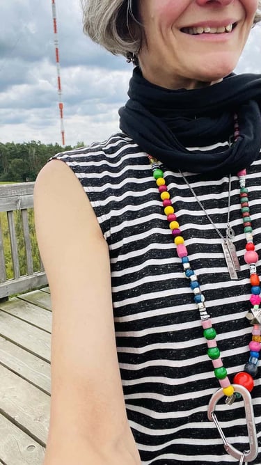 samuko wearing a striped sleeveless shirt and colorful beaded necklaces on a wooden boardwalk.