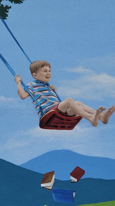 Fresque sur façade. Un garçon joue sur une balançoire au-dessus d'une pile de livres.