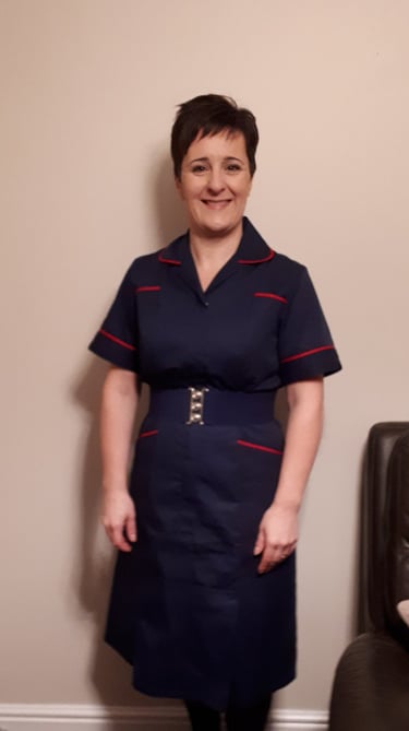 Smiling healthcare professional in a navy blue nurse uniform with red trim and a silver buckle belt.
