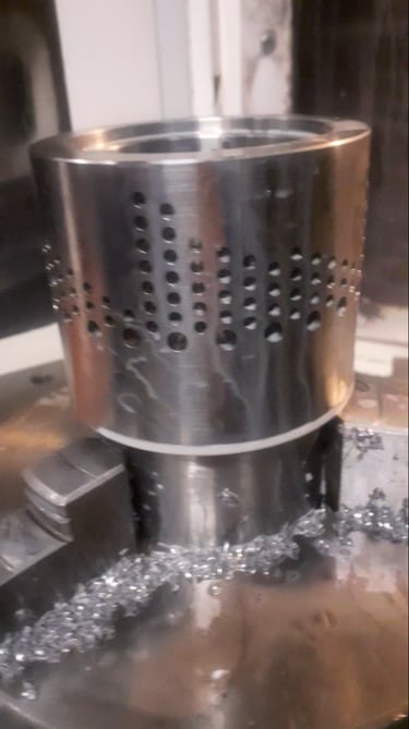 Precision CNC machined stainless steel cylindrical part with perforated hole patterns and metal shavings.