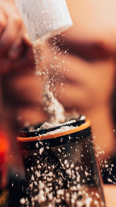 A person pouring a scoop of white whey protein powder into a fitness shaker bottle.
