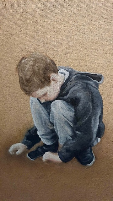 details of boy crouching. wearing blue top with hood down. has grey joggers and black pumps .