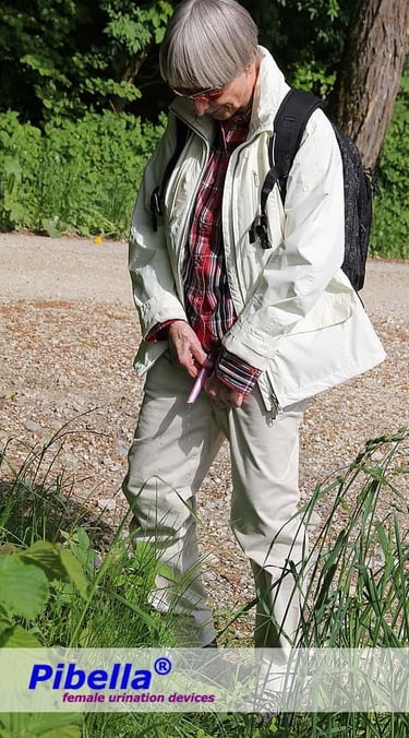Older woman using the Pibella female urination device while standing in the forest, trousers kept up.