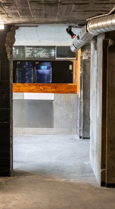 Industrial underground bar with concrete walls, metal counters, and a chalkboard drink menu.