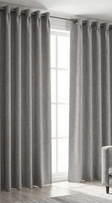 Modern grey blackout eyelet curtains hanging in a bright living room with a grey sofa.