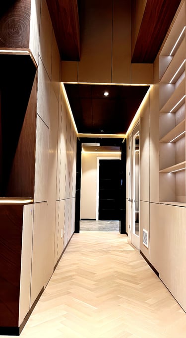 Modern luxury hallway featuring light oak herringbone wood floors, recessed LED cove lighting, and wood paneled walls.