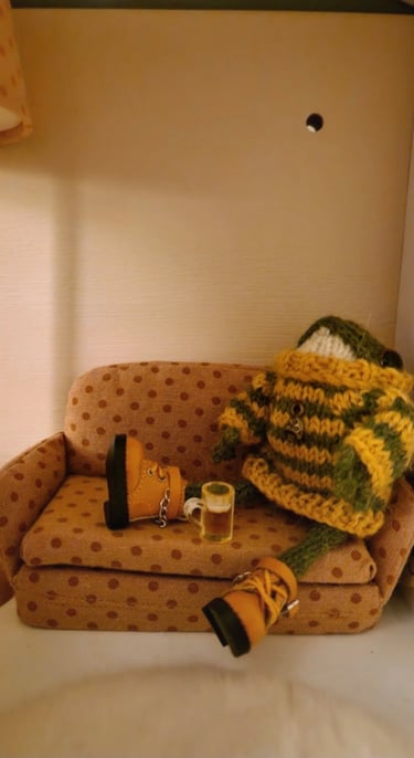 a couch with a sitting small knitted frog holding a pint of beer