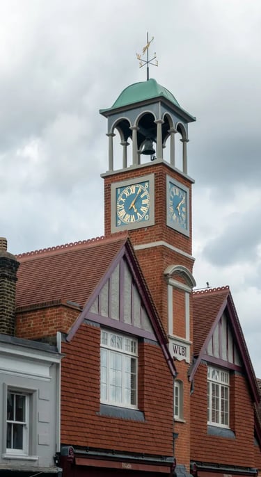 Historic red brick clock tower with a green dome and gold Roman numerals under a cloudy sky.