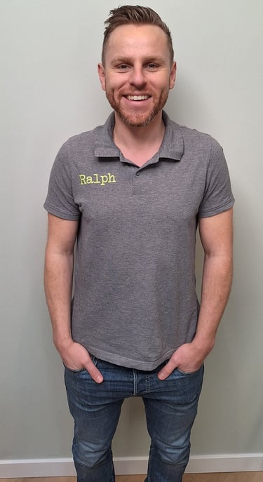 een man in een grijs shirt en broek die voor een muur staat