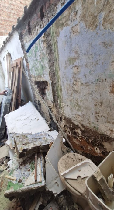 Mur extérieur très dégradé avant rénovation, avec enduit effrité, moisissures et gravats au sol.