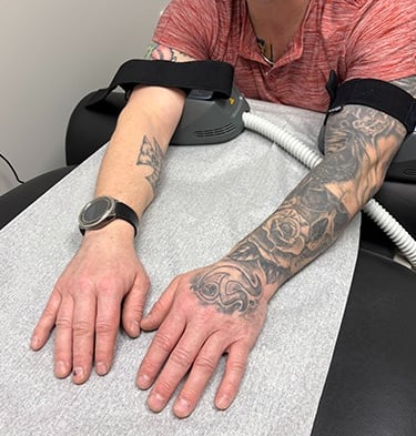 A patient in a doctors office using the BLT  Emsculpt on his arms talking to dr. aluko