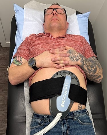 A patient in a doctors office laying on a bed using the BLT Emsculpt on his abdomen 