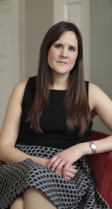 Photo of Anna Joyce CBT for insomnia therapist, sitting in red chair wearing a black geometric dress