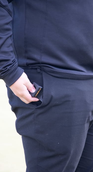 Golfer in black athletic wear placing a black and orange golf rangefinder into the right pocket of their trousers.
