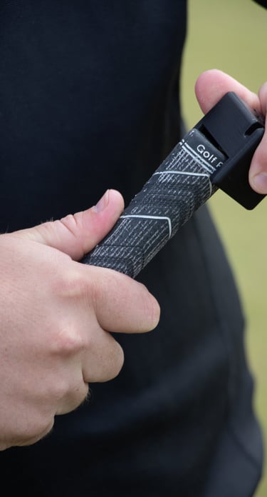 A golfer's hands adjusting a black golf grip tool, Teezup, on the handle of a club, focusing on the grip and tool in use.