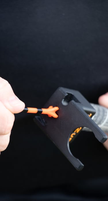 A close-up of a golfer's hand placing an orange golf tee into a 'TeeZup' tool attached to a club grip.