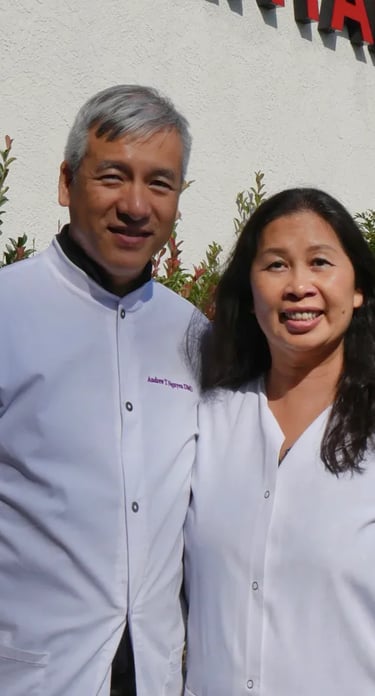 Dr. Andrew Nguyen and female colleague in white dental lab coats standing outside their clinic.