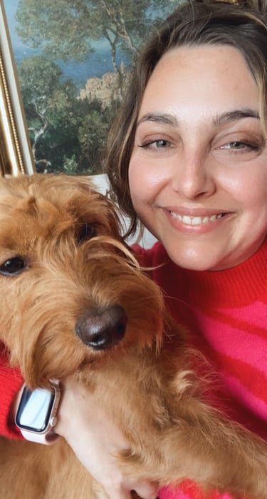 a woman in a hot pink sweater holding a miniature golden doodle with art in the background