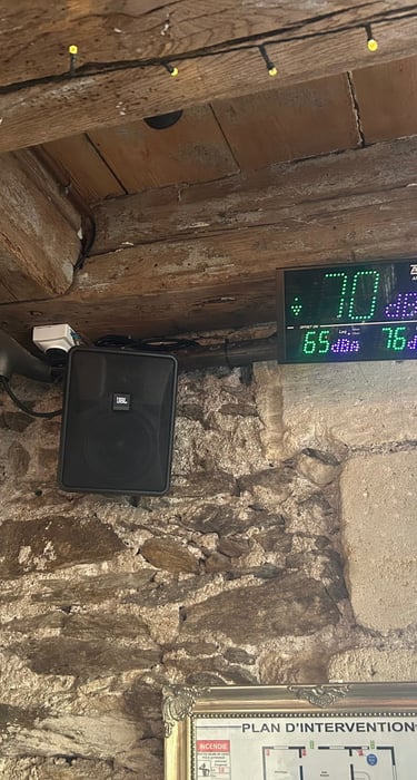 Sonmètre numérique et haut-parleur JBL monté sur un mur en pierre rustique avec des poutres en bois