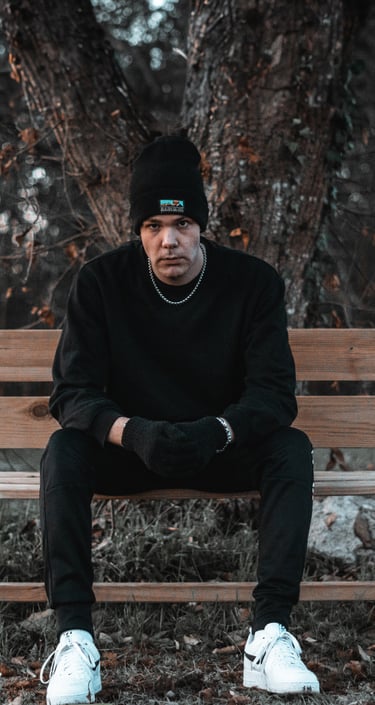 Fotografía de un hombre sentado en un banco, vestido de negro