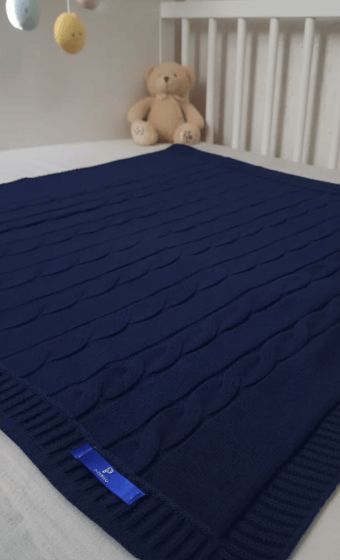 Manta Cobertor com desenho de trança em cima de um berço como ambientação