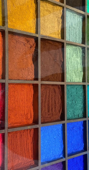 A wooden display case featuring vibrant rows of colorful artist pigment powders in a variety of hues.