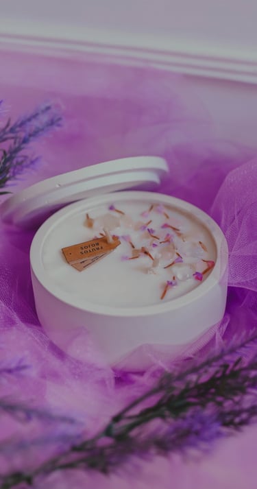 Vela de soja perfumada en un tarro de cerámica blanca decorado con lavanda sobre tul morado.