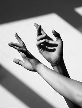 A black and white image of hands with shadow's cast on a wall.
