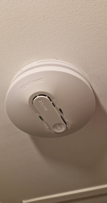 White Clipsal smoke alarm with green power indicator light installed on a ceiling.