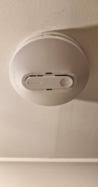 White Clipsal smoke alarm mounted on a ceiling with power and battery indicators.