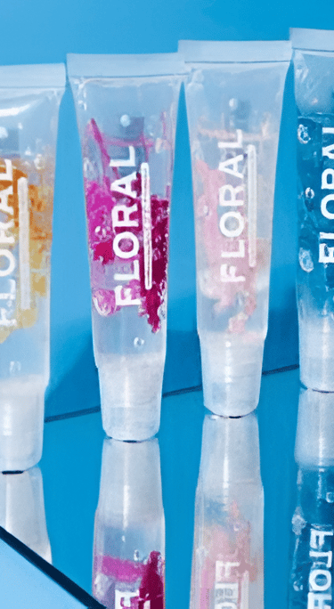 Cuatro tubos transparentes de brillo labial con motivos florales, pétalos de flores y burbujas sobre